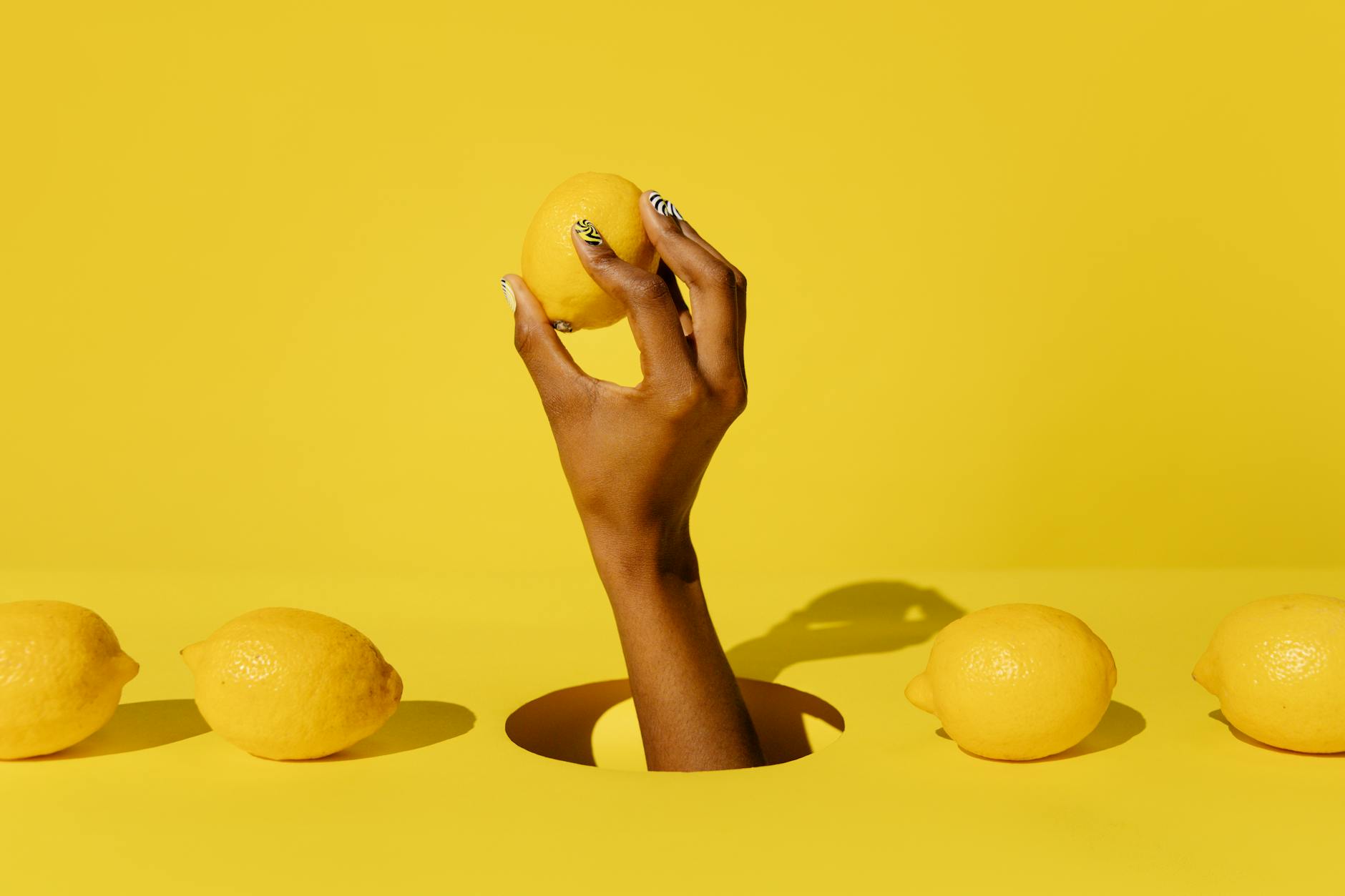 Hand holding a fresh lemon against a bright yellow background, symbolizing the slow, intentional build of arousal