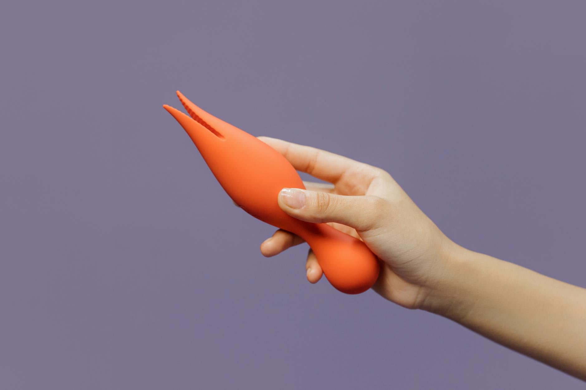 Close-up of a hand holding a lemon-colored vibrator against a minimalist purple backdrop