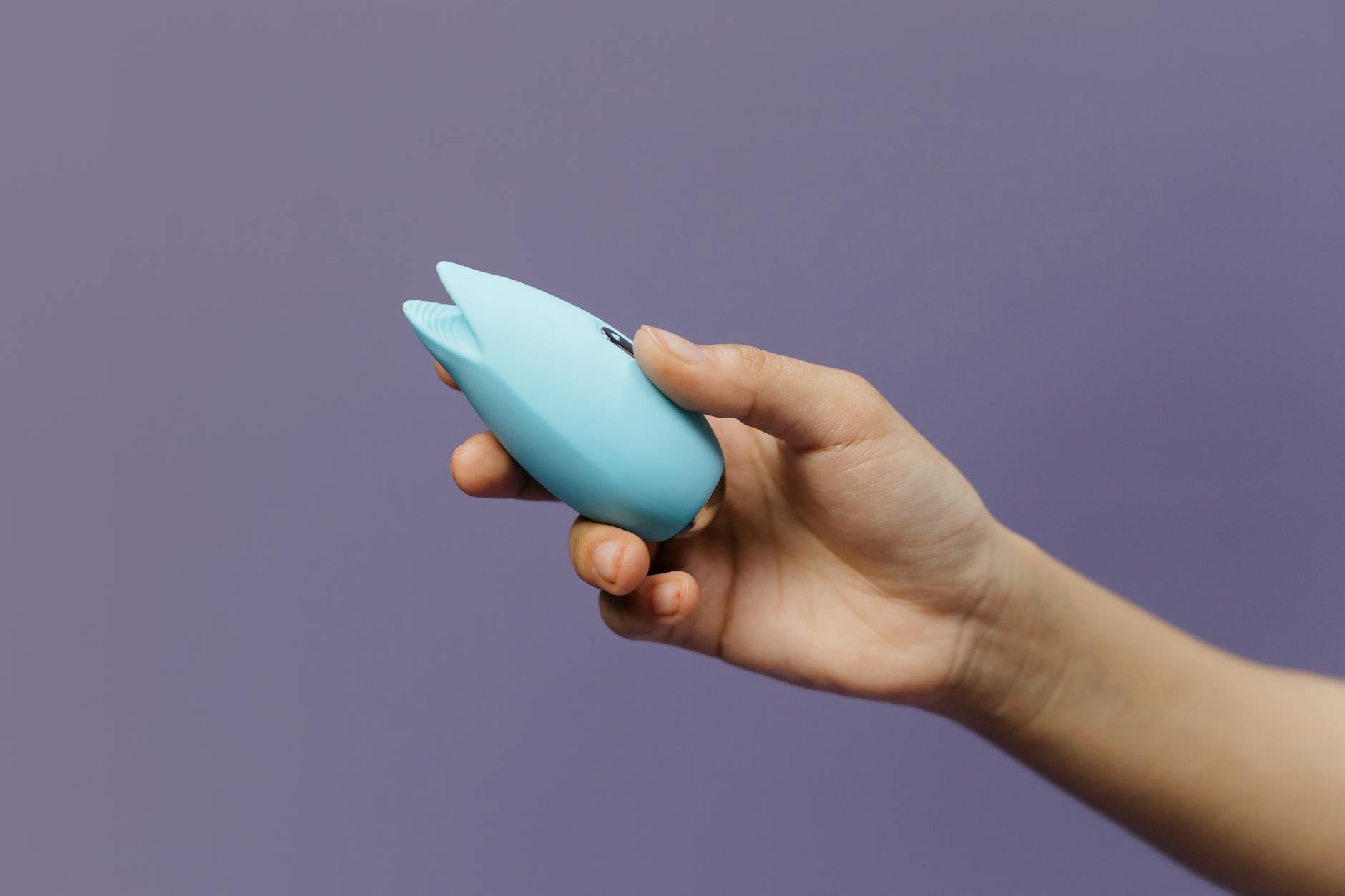 A blue silicone clitoral vibrator held in hand, representing tools for sensual self-discovery and intimate reconnection