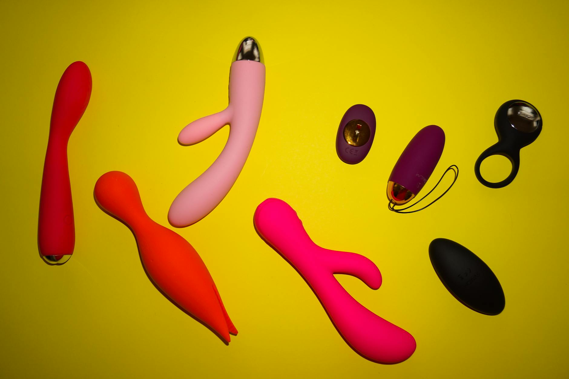 Vibrant arrangement of various colorful clitoral vibrators and sex toys on a bright yellow background